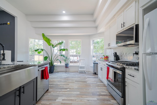 kitchen with light stone counters, white cabinetry, stainless steel appliances, and light hardwood / wood-style flooring