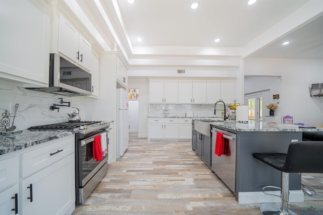 kitchen featuring a kitchen bar, white cabinetry, light stone counters, and appliances with stainless steel finishes