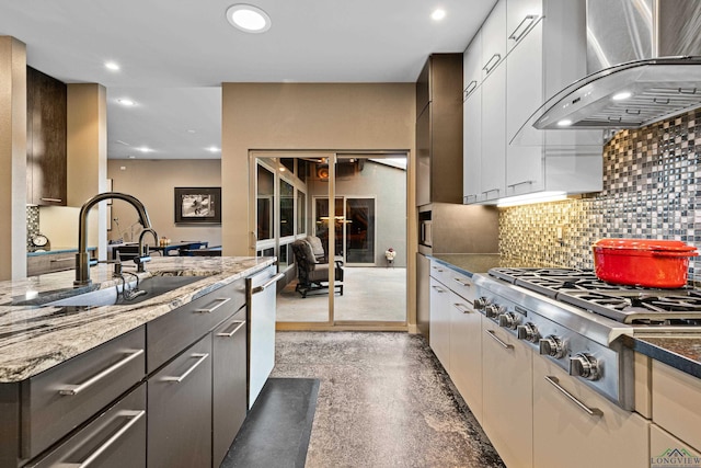 kitchen featuring sink, dark stone counters, wall chimney range hood, and appliances with stainless steel finishes