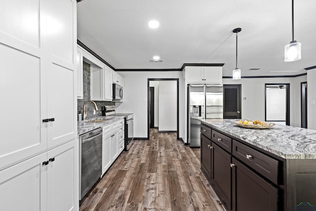 kitchen with pendant lighting, sink, light stone countertops, white cabinetry, and stainless steel appliances