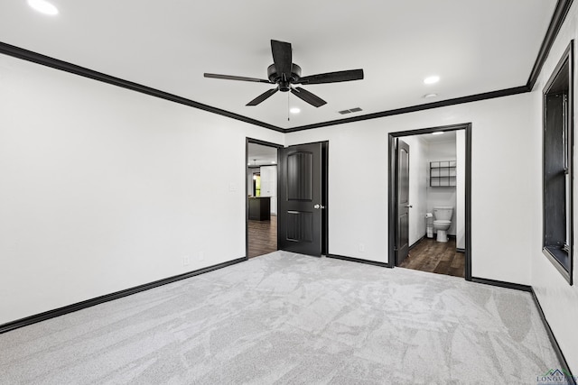 unfurnished bedroom featuring ensuite bathroom, dark carpet, ceiling fan, and ornamental molding