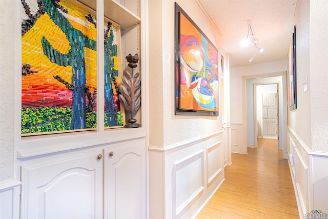 hall featuring light hardwood / wood-style flooring, track lighting, and a textured ceiling