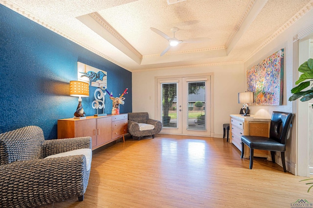 living area featuring french doors, a textured ceiling, a tray ceiling, ceiling fan, and light hardwood / wood-style floors