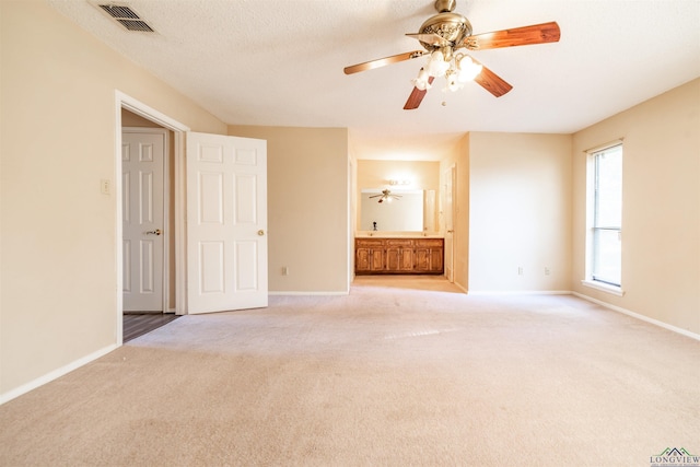 unfurnished bedroom featuring ensuite bathroom, light colored carpet, and ceiling fan