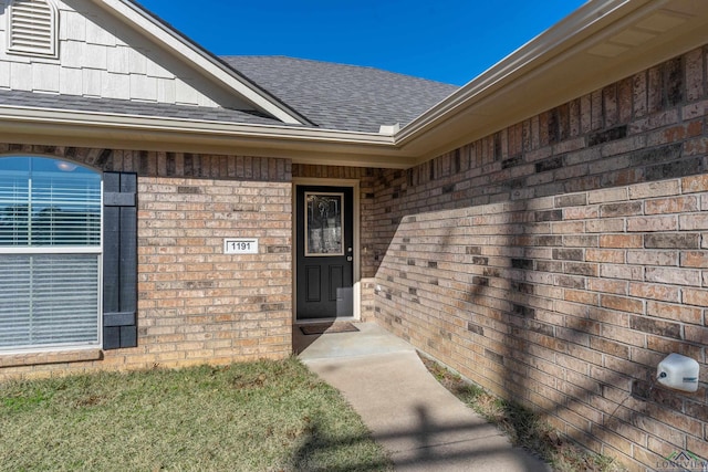 property entrance with a shingled roof and brick siding