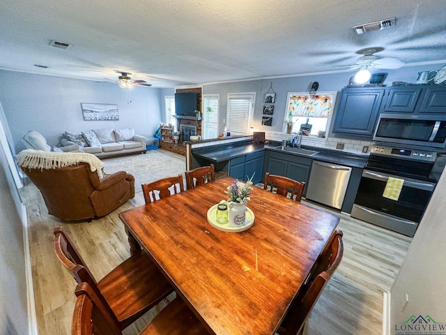 902 Warren Dr, Marshall, TX 75672 - dining area featuring a ceiling fan, light wood finished floors, a textured ceiling, and a glass covered fireplace