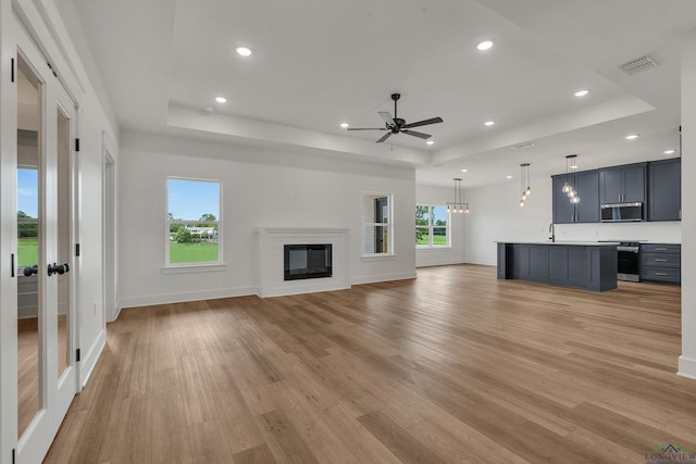1507 Wellington Ln, Longview, TX 75605 - unfurnished living room featuring a raised ceiling, light wood finished floors, a ceiling fan, recessed lighting, and a glass covered fireplace