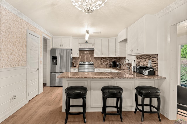 kitchen with kitchen peninsula, appliances with stainless steel finishes, white cabinets, and a kitchen breakfast bar