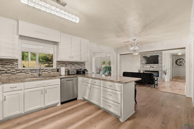 kitchen featuring kitchen peninsula, stainless steel dishwasher, decorative light fixtures, a fireplace, and white cabinetry