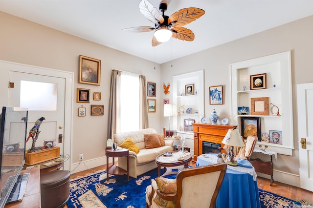 living room with hardwood / wood-style flooring, built in shelves, ceiling fan, and a fireplace