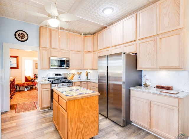 kitchen with appliances with stainless steel finishes, light stone counters, light brown cabinets, a center island, and light hardwood / wood-style floors