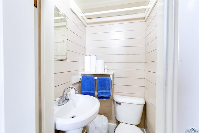 bathroom featuring toilet, sink, and wooden walls