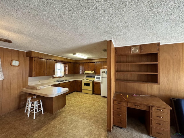 kitchen with kitchen peninsula, white appliances, wooden walls, sink, and a breakfast bar area