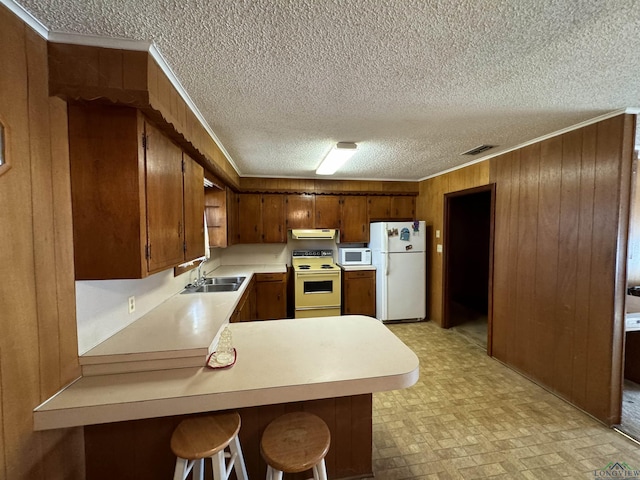 kitchen with sink, kitchen peninsula, wood walls, white appliances, and a kitchen bar