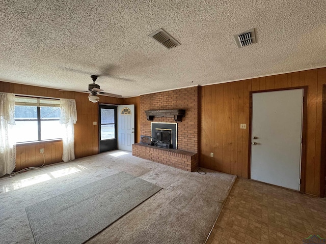 unfurnished living room with ceiling fan, carpet floors, a fireplace, and wooden walls