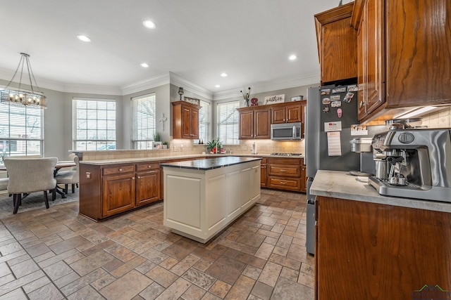 kitchen with a kitchen island, appliances with stainless steel finishes, backsplash, brown cabinetry, and crown molding