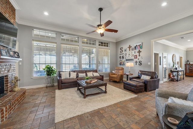 living room featuring ceiling fan, a fireplace, baseboards, stone tile flooring, and crown molding