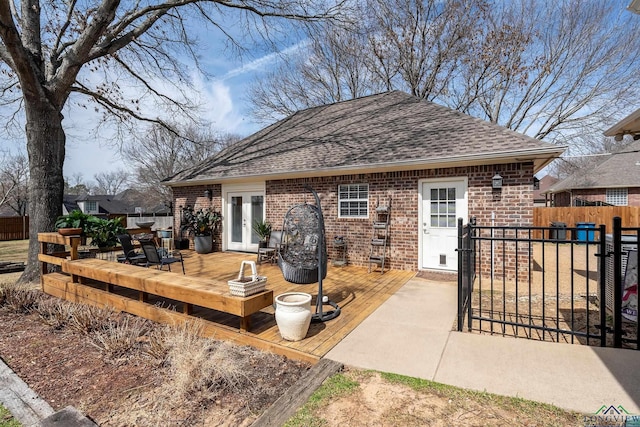 rear view of property with brick siding, fence, french doors, roof with shingles, and a wooden deck