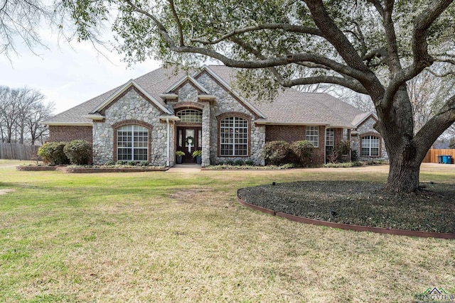 french country style house featuring brick siding, a shingled roof, and a front yard