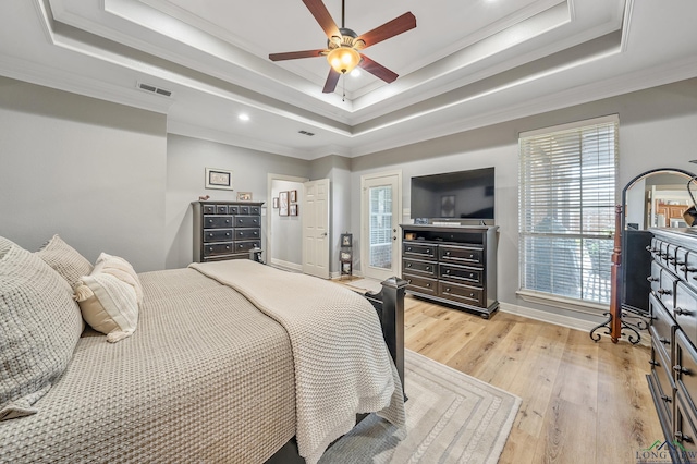 bedroom featuring visible vents, a ceiling fan, light wood-style flooring, a tray ceiling, and crown molding