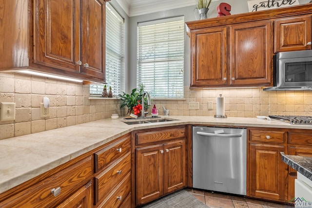 kitchen with decorative backsplash, appliances with stainless steel finishes, brown cabinets, crown molding, and a sink