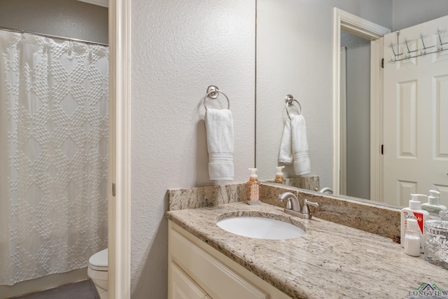 bathroom with a textured wall, vanity, toilet, and a shower with curtain