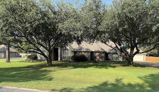 view of property hidden behind natural elements featuring a garage, a front yard, and fence