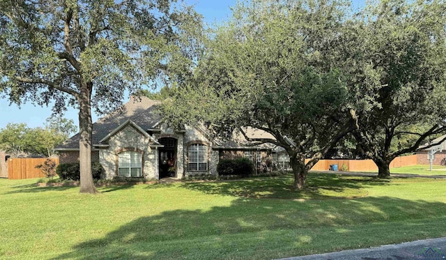 view of front of home with a front yard, stone siding, and fence