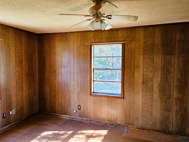 empty room with ceiling fan, wood walls, wood-type flooring, and a textured ceiling