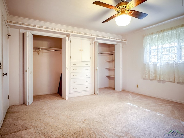 unfurnished bedroom with two closets, crown molding, ceiling fan, and light colored carpet