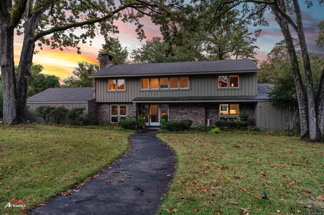 traditional-style home with a chimney, brick siding, driveway, roof with shingles, and a front lawn