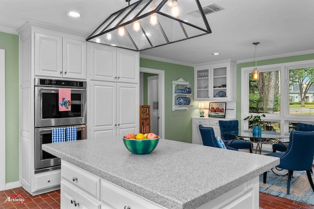 kitchen featuring ornamental molding, stainless steel double oven, decorative light fixtures, white cabinets, and a center island