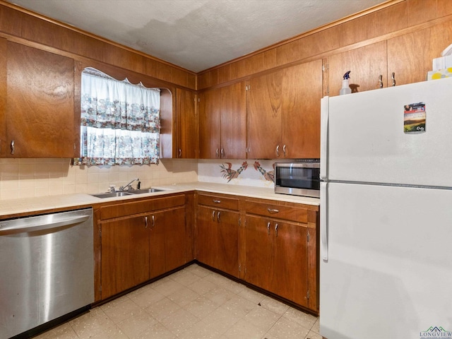 kitchen featuring brown cabinets, light countertops, freestanding refrigerator, a sink, and dishwasher