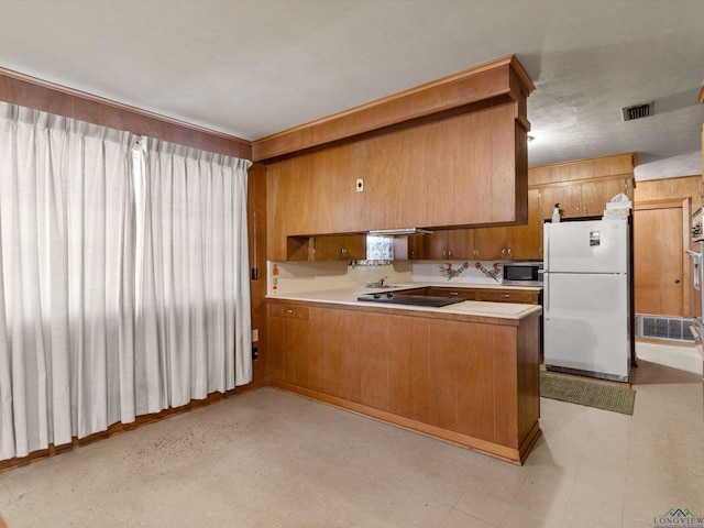 kitchen with freestanding refrigerator, light countertops, stainless steel microwave, and a peninsula