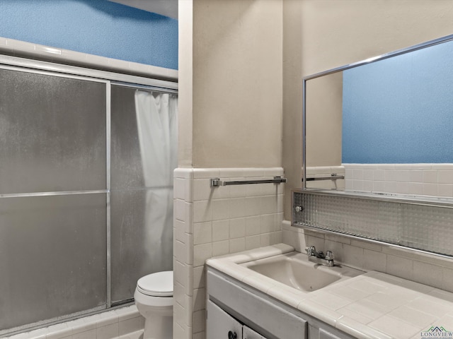 full bathroom with wainscoting, toilet, vanity, a shower stall, and tile walls