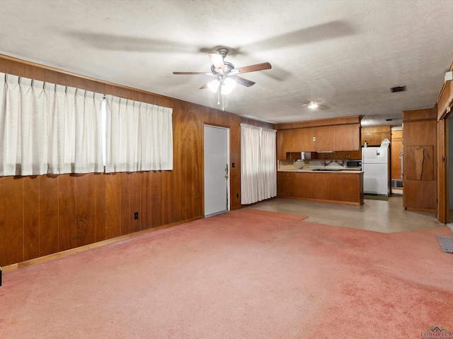 kitchen featuring brown cabinets, light colored carpet, freestanding refrigerator, wooden walls, and a peninsula