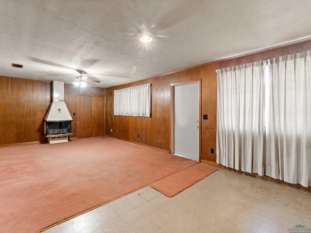 interior space with visible vents, a ceiling fan, wood walls, a textured ceiling, and tile patterned floors