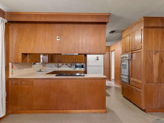 kitchen with appliances with stainless steel finishes, brown cabinets, light countertops, and a peninsula