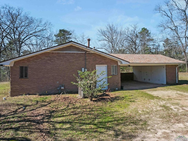 view of side of property featuring an attached carport, brick siding, a yard, and dirt driveway