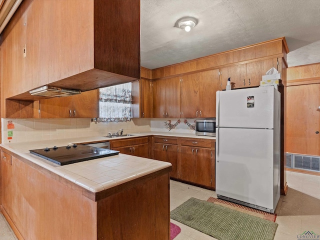 kitchen featuring black electric stovetop, visible vents, stainless steel microwave, freestanding refrigerator, and a peninsula