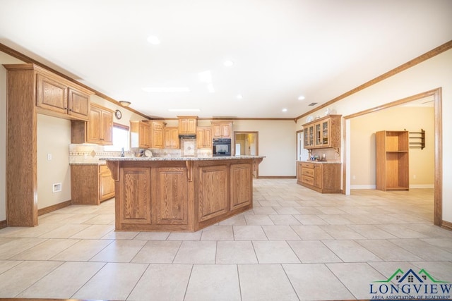 kitchen featuring light stone counters, backsplash, crown molding, black oven, and a kitchen island