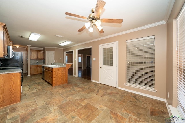 kitchen with stone tile floors, a center island with sink, ornamental molding, and brown cabinetry