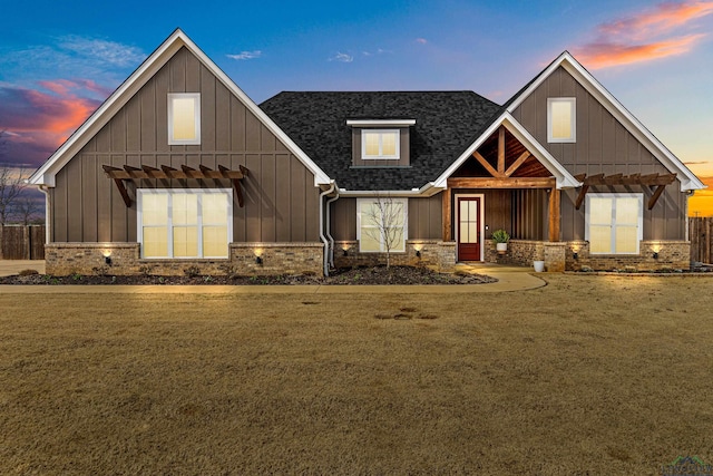 view of front of property with board and batten siding, stone siding, a shingled roof, and a front lawn