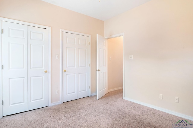 unfurnished bedroom with light colored carpet and two closets