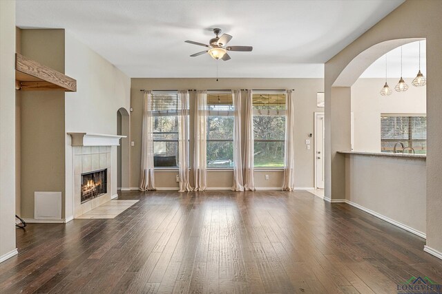 unfurnished living room featuring a tiled fireplace, ceiling fan, and dark wood-type flooring