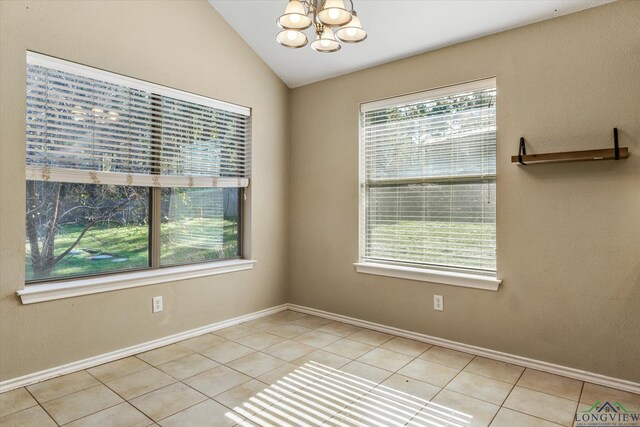 tiled empty room featuring plenty of natural light, lofted ceiling, and an inviting chandelier