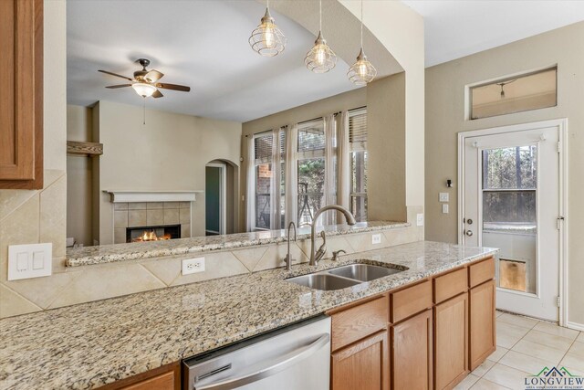 kitchen featuring light stone countertops, dishwasher, sink, pendant lighting, and a tiled fireplace