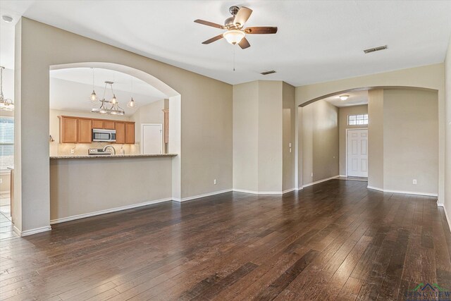 unfurnished living room with vaulted ceiling, ceiling fan with notable chandelier, and dark hardwood / wood-style floors