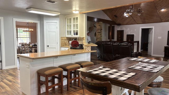 interior space featuring an inviting chandelier, lofted ceiling, glass insert cabinets, wood finished floors, and light countertops