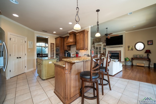 kitchen featuring light stone countertops, premium range hood, a center island, a breakfast bar area, and light tile patterned flooring